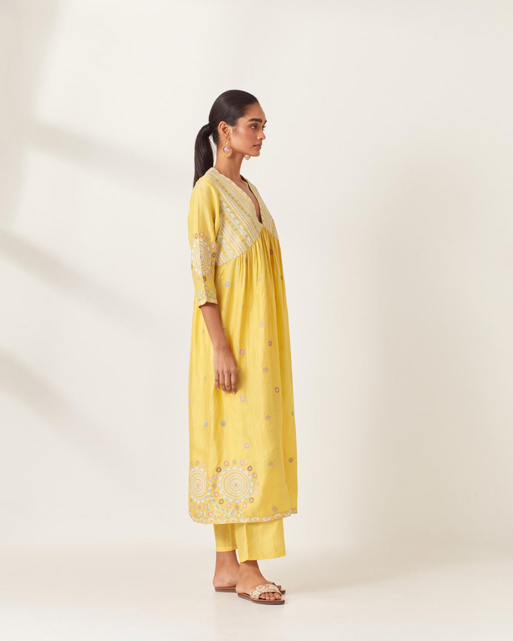 Yellow silk kurta dress set with appliqué stripes along with aari threadwork flowers and floral trellises along with a circular appliqued motif and fine gathers at empire line.