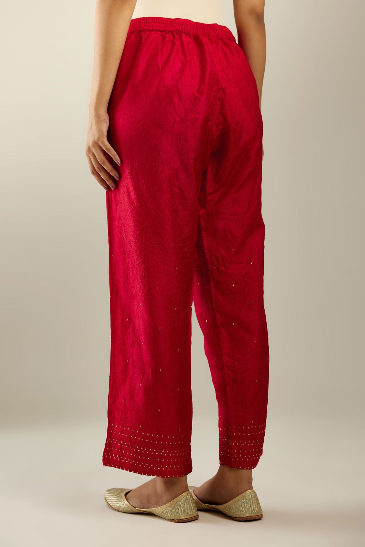 Red hand crushed pure silk straight pants with gold sequins at hem in horizontal lines formation and side pockets.