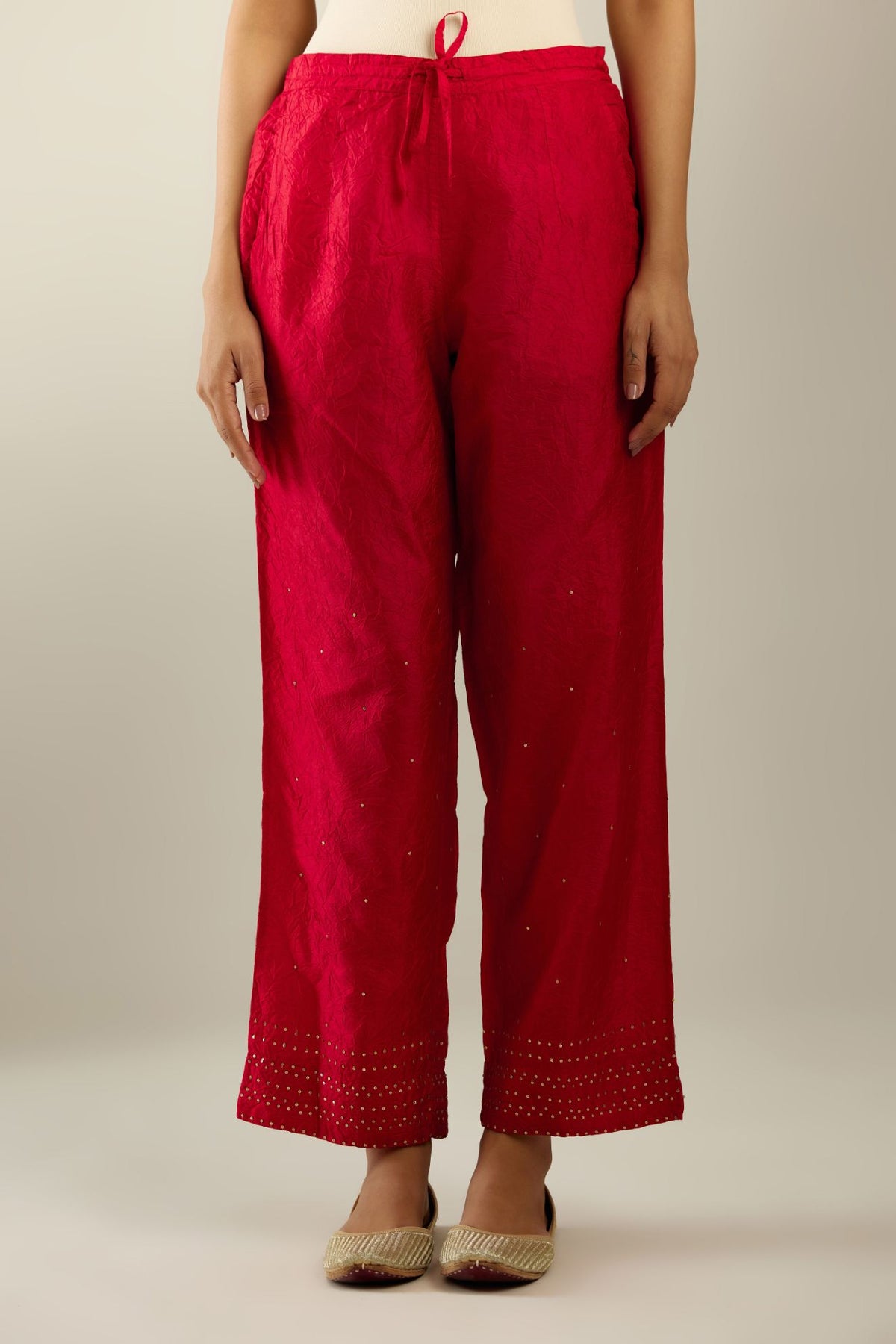 Red hand crushed pure silk straight pants with gold sequins at hem in horizontal lines formation and side pockets.