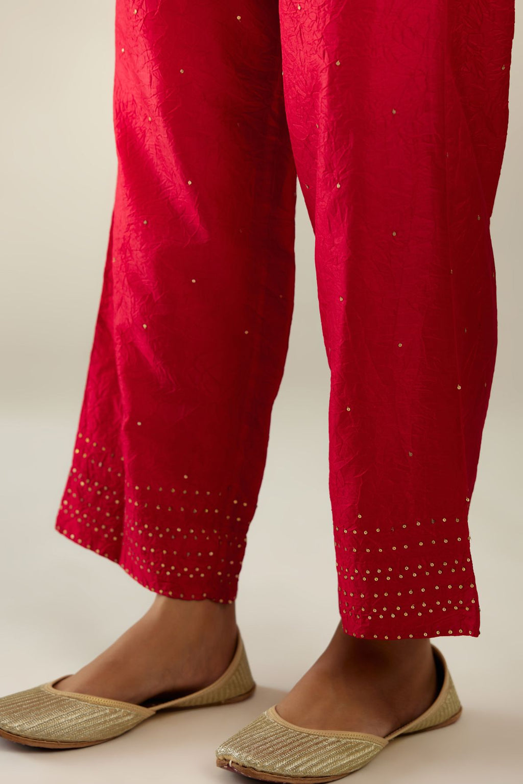 Red hand crushed pure silk straight pants with gold sequins at hem in horizontal lines formation and side pockets.