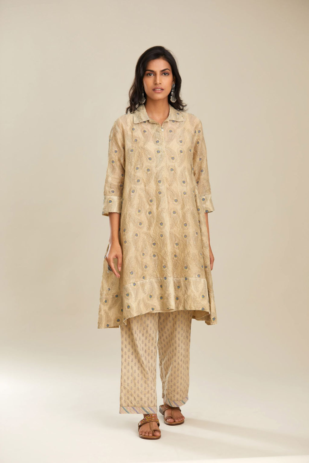 Beige hand block printed silk chanderi  A-line short shirt kurta with silk fabric detailing at hem and front placket that ends with a box pleat, paired with beige hand block printed straight pants with striped fabric attached at bottom.