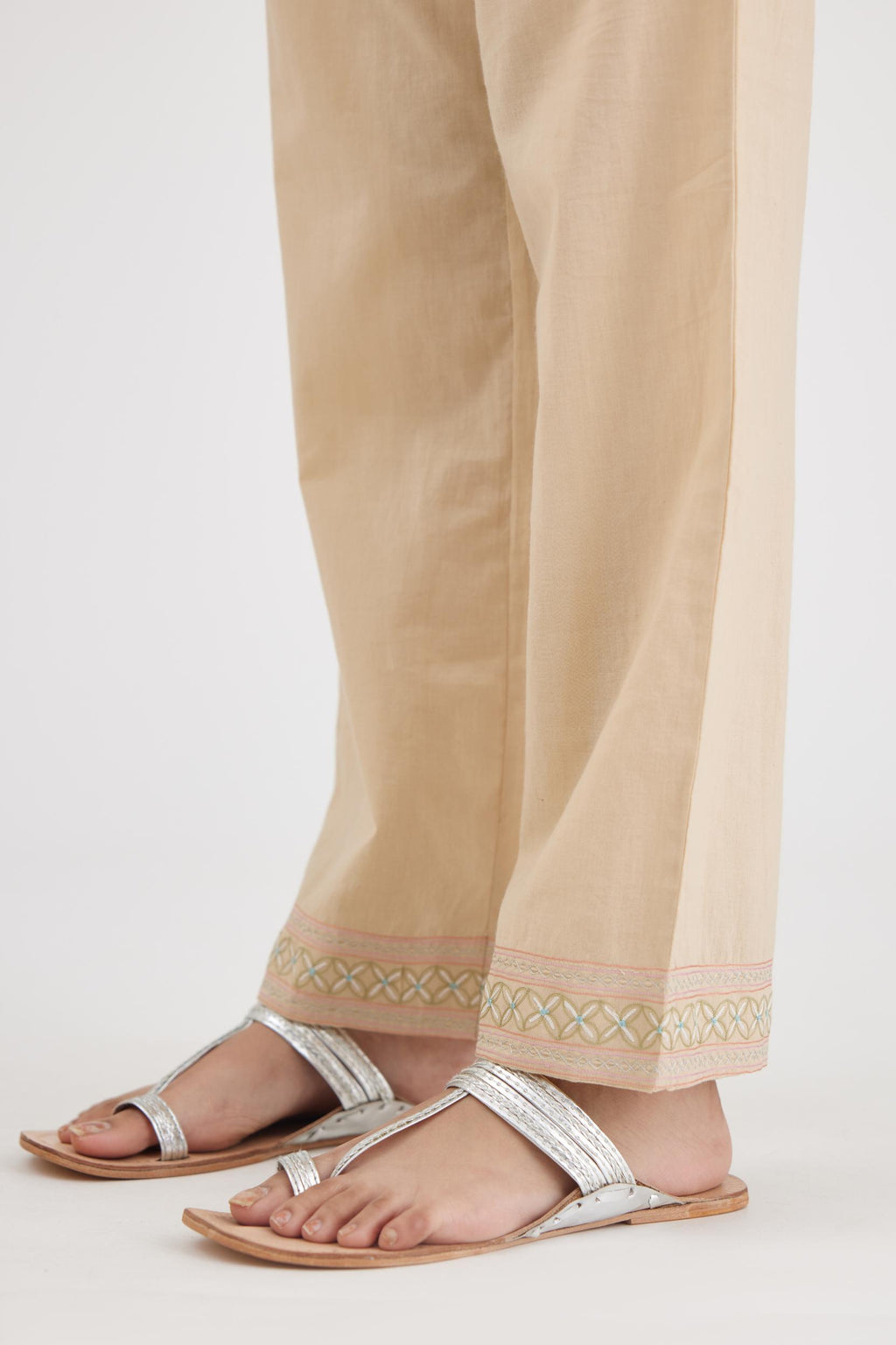Beige cotton straight pants with multi colored thread embroidery, highlighted with silver zari embroidery at bottom hem