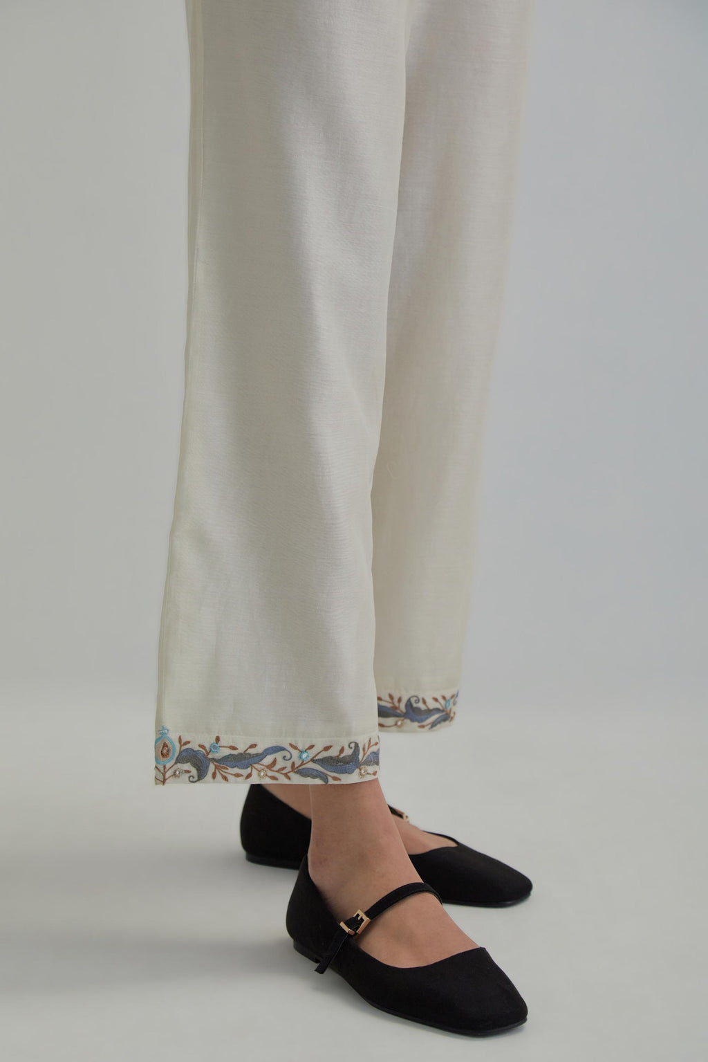 Off white silk Chanderi straight pants with earthy coloured Aari work at hem.