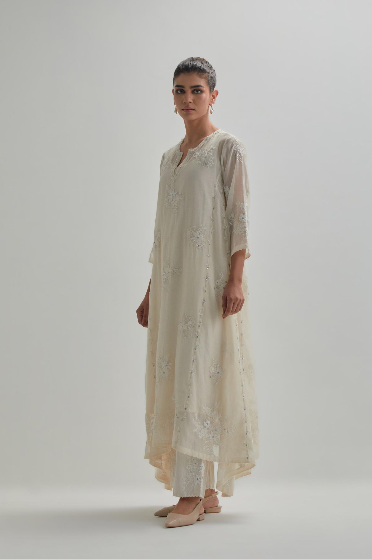 Off-white cotton Chanderi kurta set with asymmetric hem and all-over appliqué flowers, highlighted with sequins and beads.
