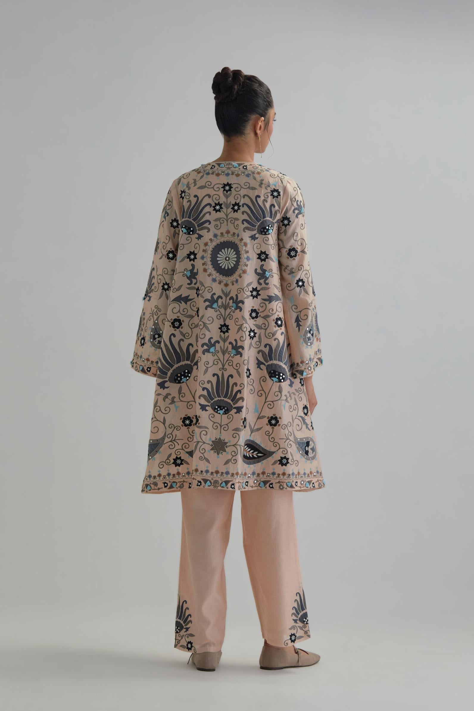 Pink short front open A-line jacket, fully embroidered with bold appliqué flowers, earthy-coloured Aari thread work and silk tassels, paired with Pink silk Chanderi straight pants with earthy coloured appliqué at hem.