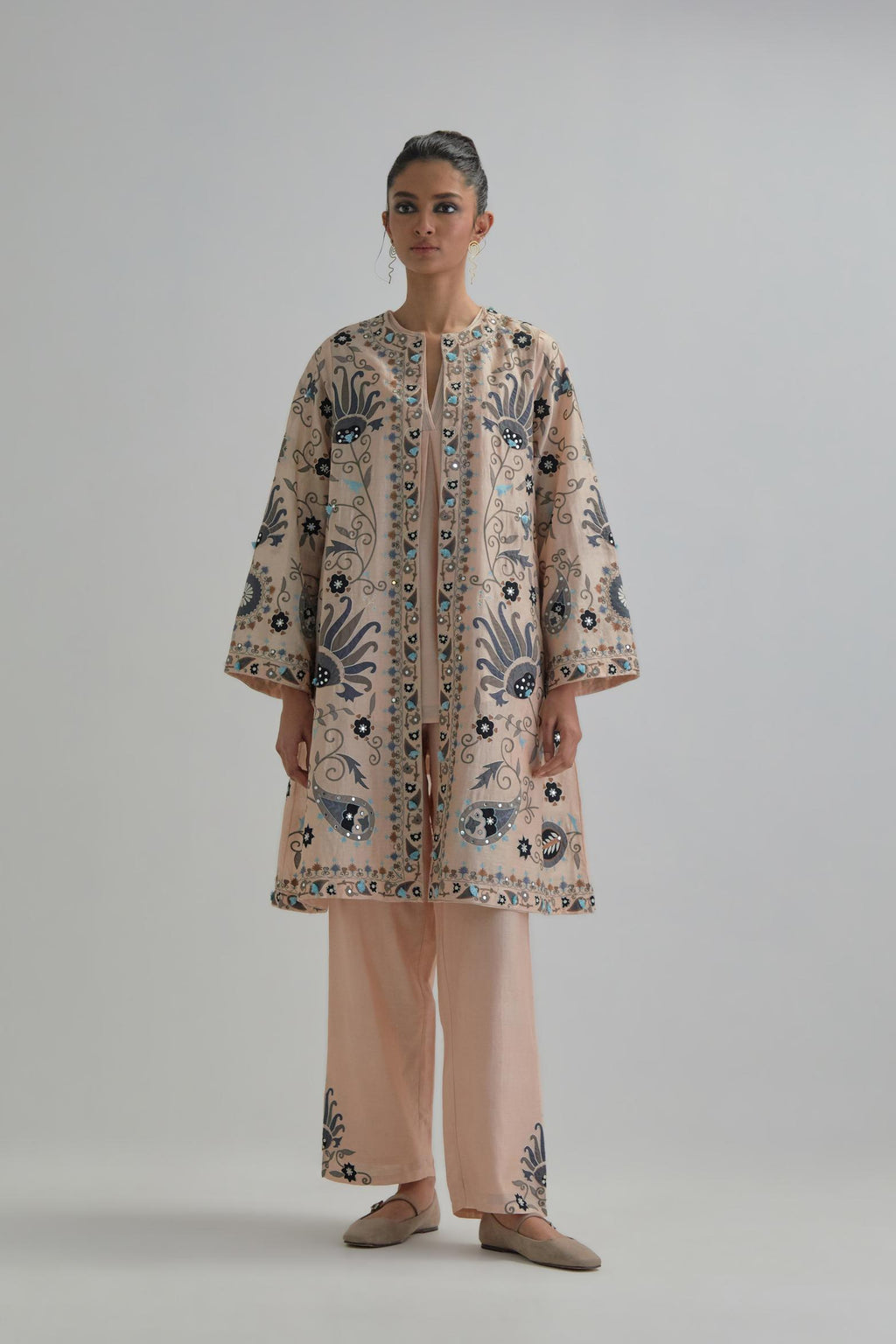Pink short front open A-line jacket, fully embroidered with bold appliqué flowers, earthy-coloured Aari thread work and silk tassels, paired with Pink silk Chanderi straight pants with earthy coloured appliqué at hem.