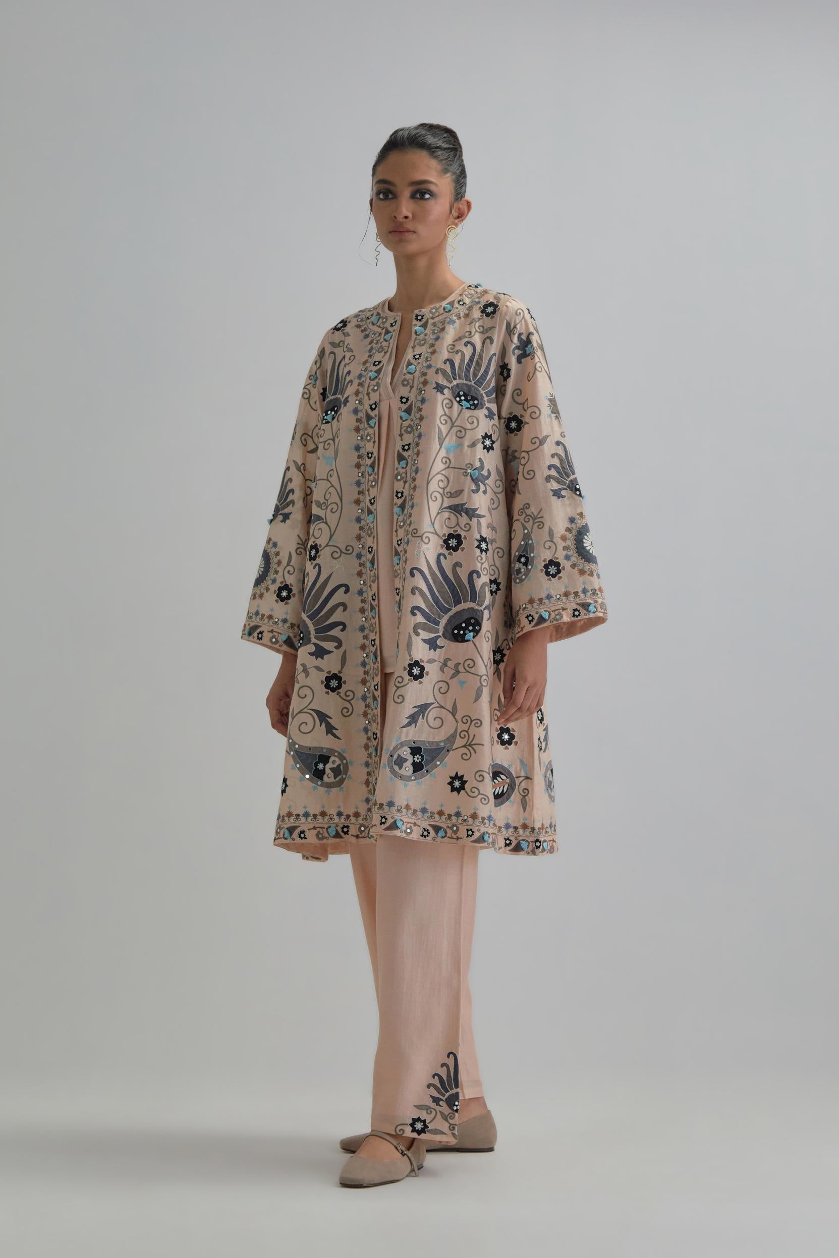Pink short front open A-line jacket, fully embroidered with bold appliqué flowers, earthy-coloured Aari thread work and silk tassels, paired with Pink silk Chanderi straight pants with earthy coloured appliqué at hem.