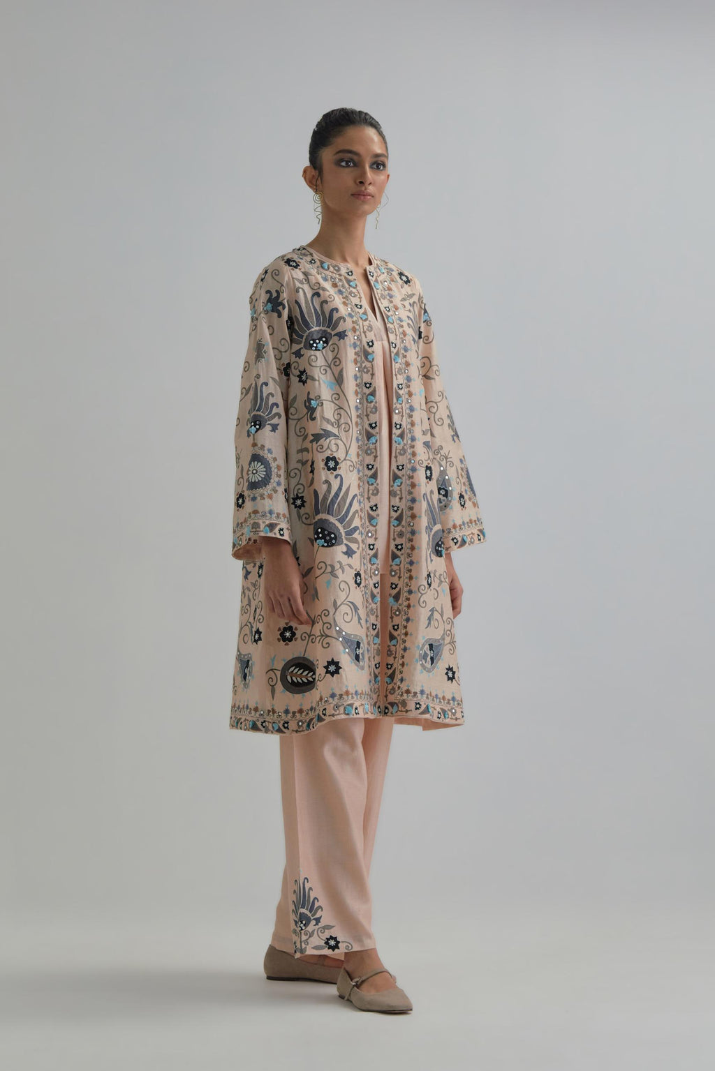 Pink short front open A-line jacket, fully embroidered with bold appliqué flowers, earthy-coloured Aari thread work and silk tassels, paired with Pink silk Chanderi straight pants with earthy coloured appliqué at hem.