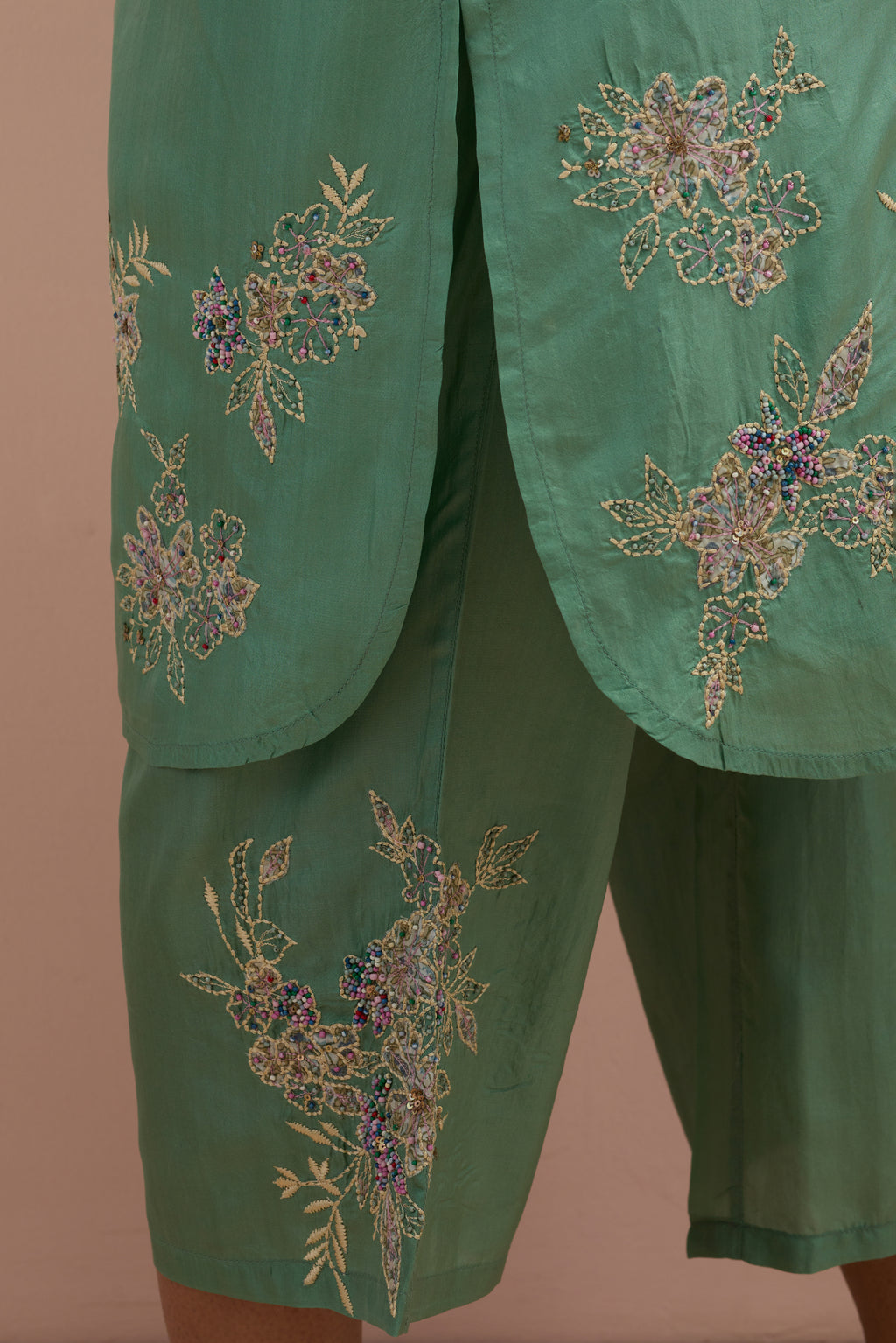 Jade green silk short shirt kurta with all-over hand block printed appliqué, highlighted with sequins and multi colored beads, paired with jade green silk ankle length straight pants with hand block printed appliqué motifs at the sides.