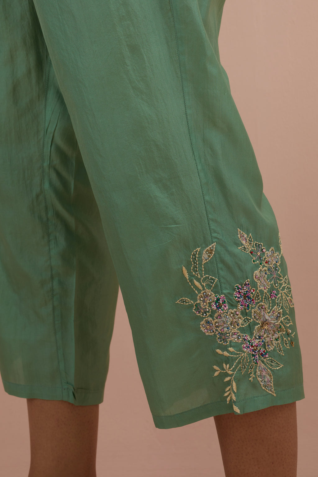 Jade green silk ankle length straight pants with hand block printed appliqué motifs at the sides, highlighted with sequins and multi-colored beads.