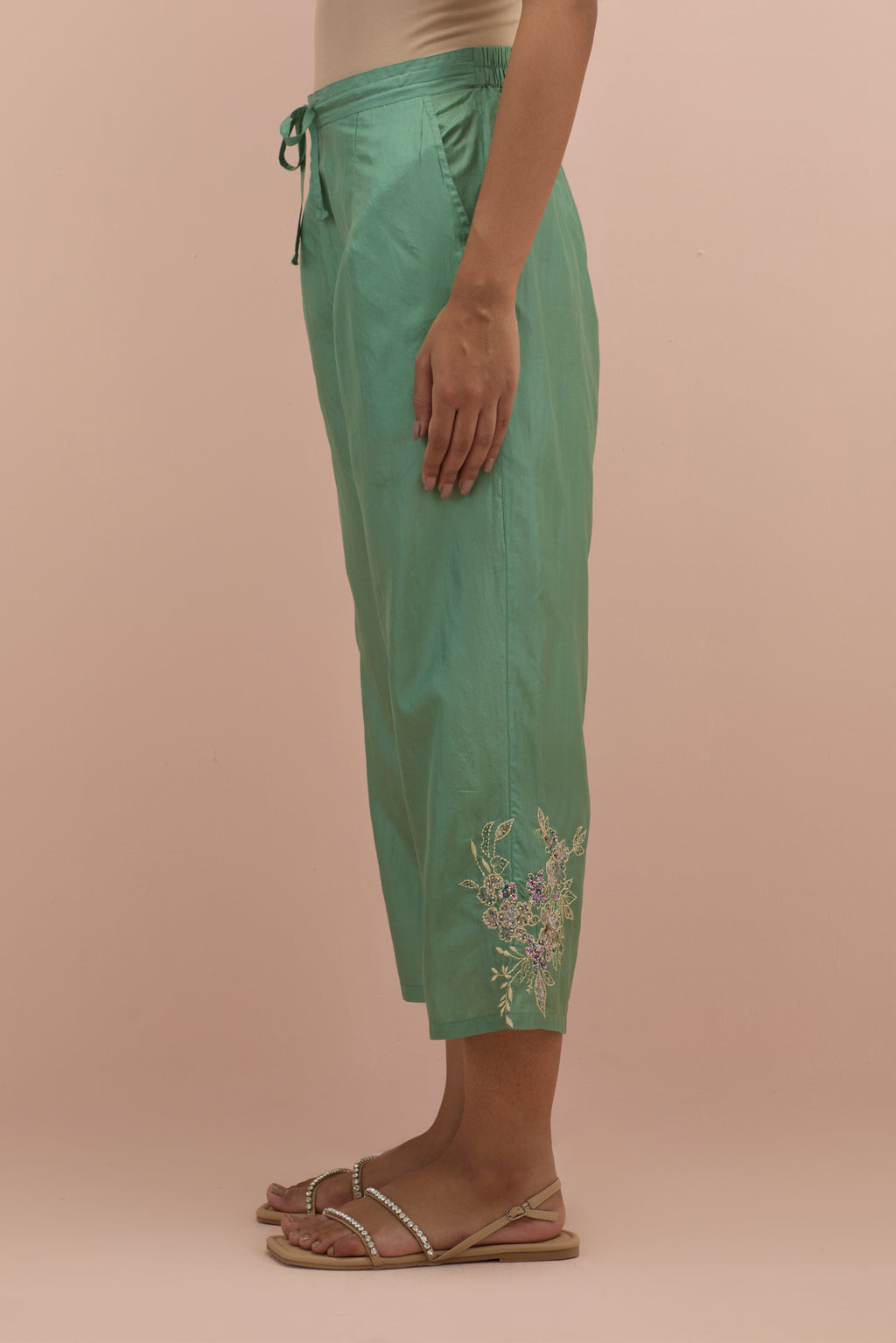 Jade green silk ankle length straight pants with hand block printed appliqué motifs at the sides, highlighted with sequins and multi-colored beads.