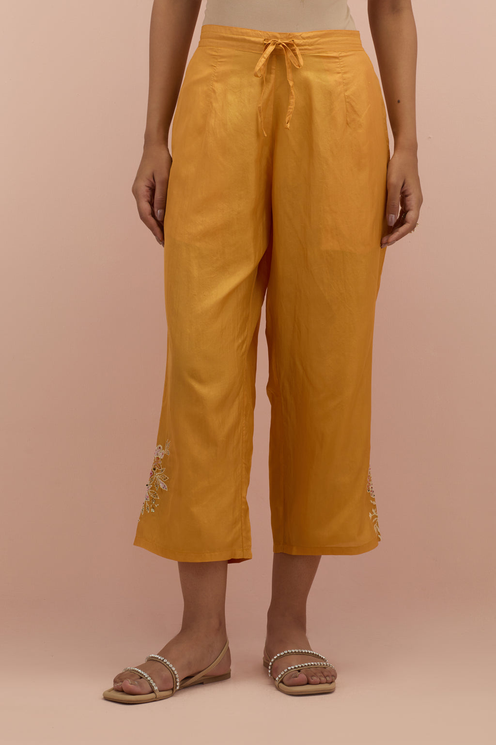 Amber silk ankle length straight pants with hand block printed appliqué motifs at the sides, highlighted with sequins and multi-colored beads.