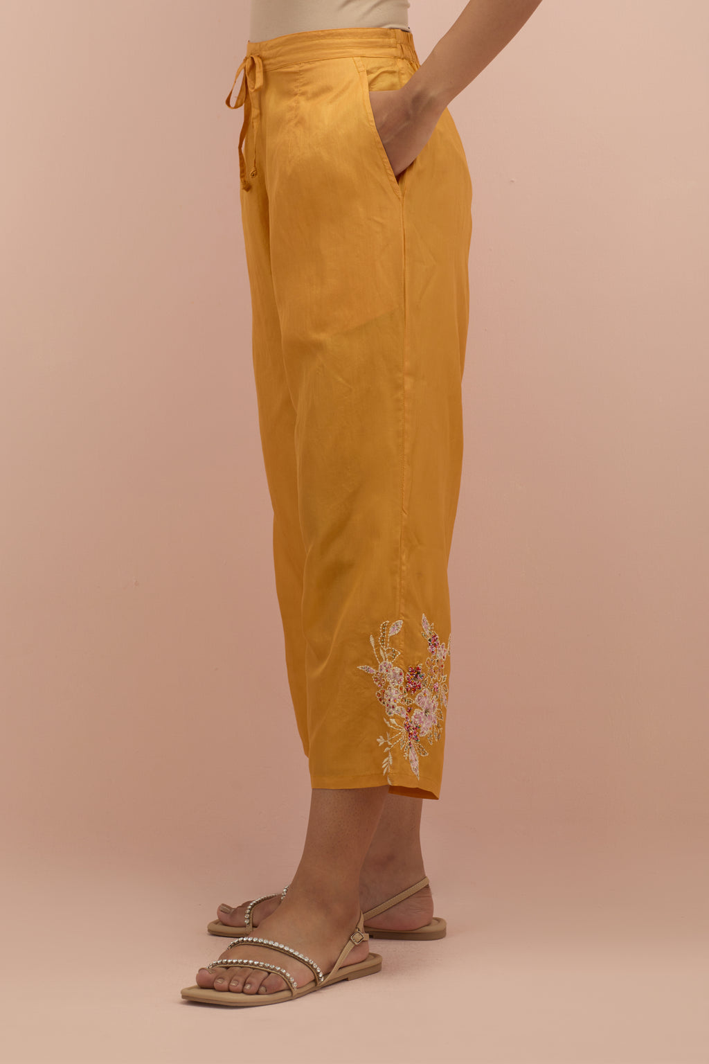 Amber silk ankle length straight pants with hand block printed appliqué motifs at the sides, highlighted with sequins and multi-colored beads.