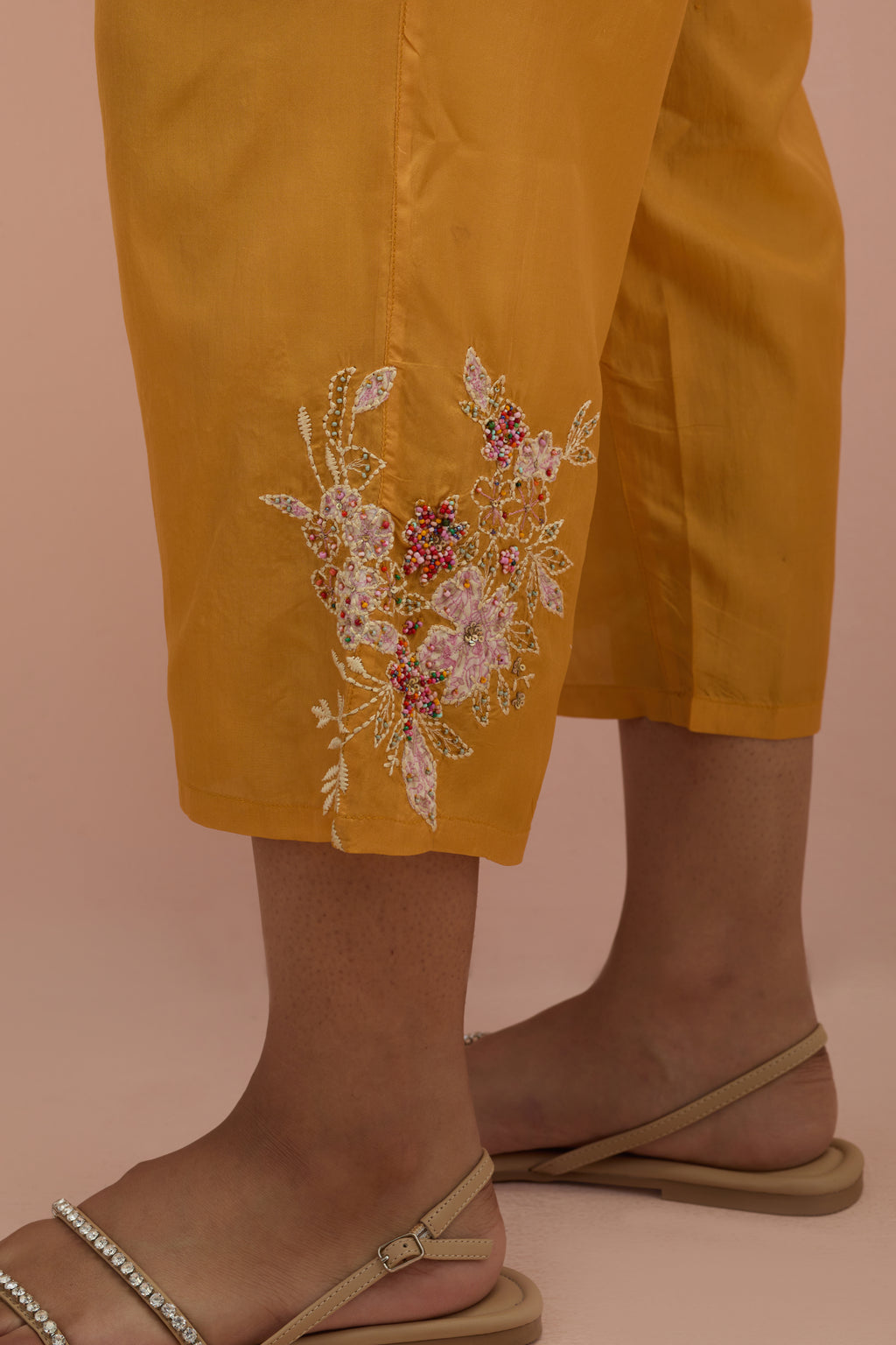 Amber silk ankle length straight pants with hand block printed appliqué motifs at the sides, highlighted with sequins and multi-colored beads.