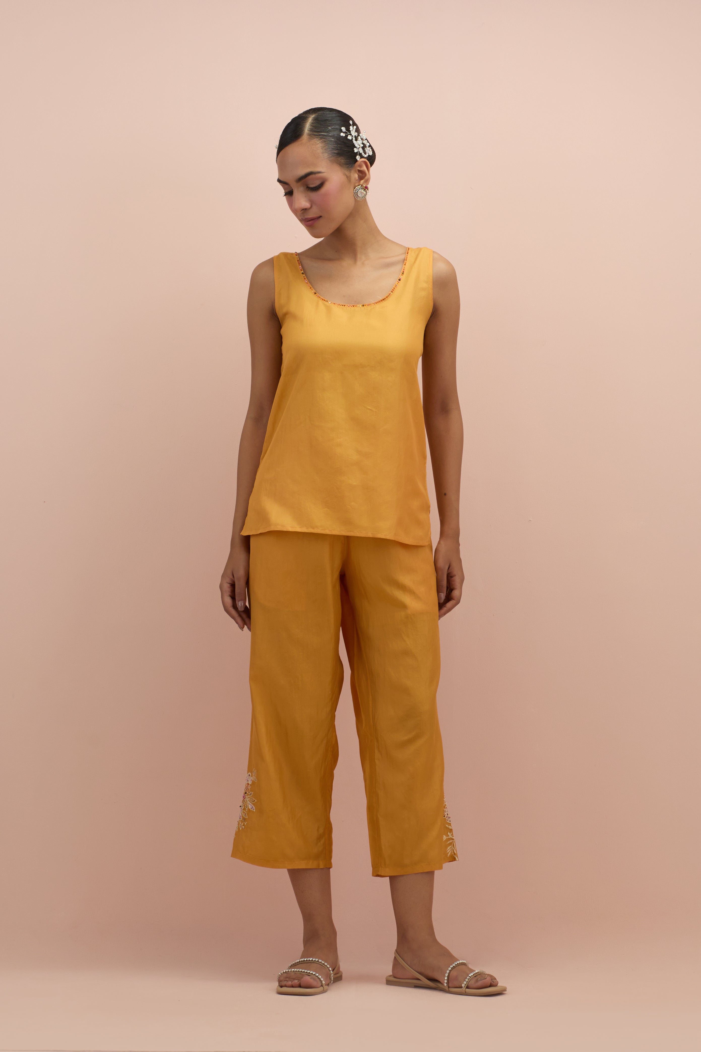 Amber silk short top with hand block printed appliqué motifs and delicate embroidered flowers, highlighted with sequins and multi-colored beads, paired with amber silk ankle length straight pants.