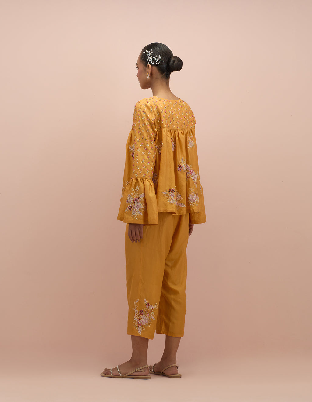 Amber silk short top with hand block printed appliqué motifs and delicate embroidered flowers, highlighted with sequins and multi-colored beads, paired with amber silk ankle length straight pants.