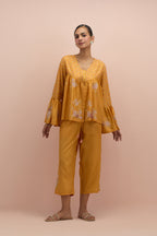 Amber silk short top with hand block printed appliqué motifs and delicate embroidered flowers, highlighted with sequins and multi-colored beads, paired with amber silk ankle length straight pants.