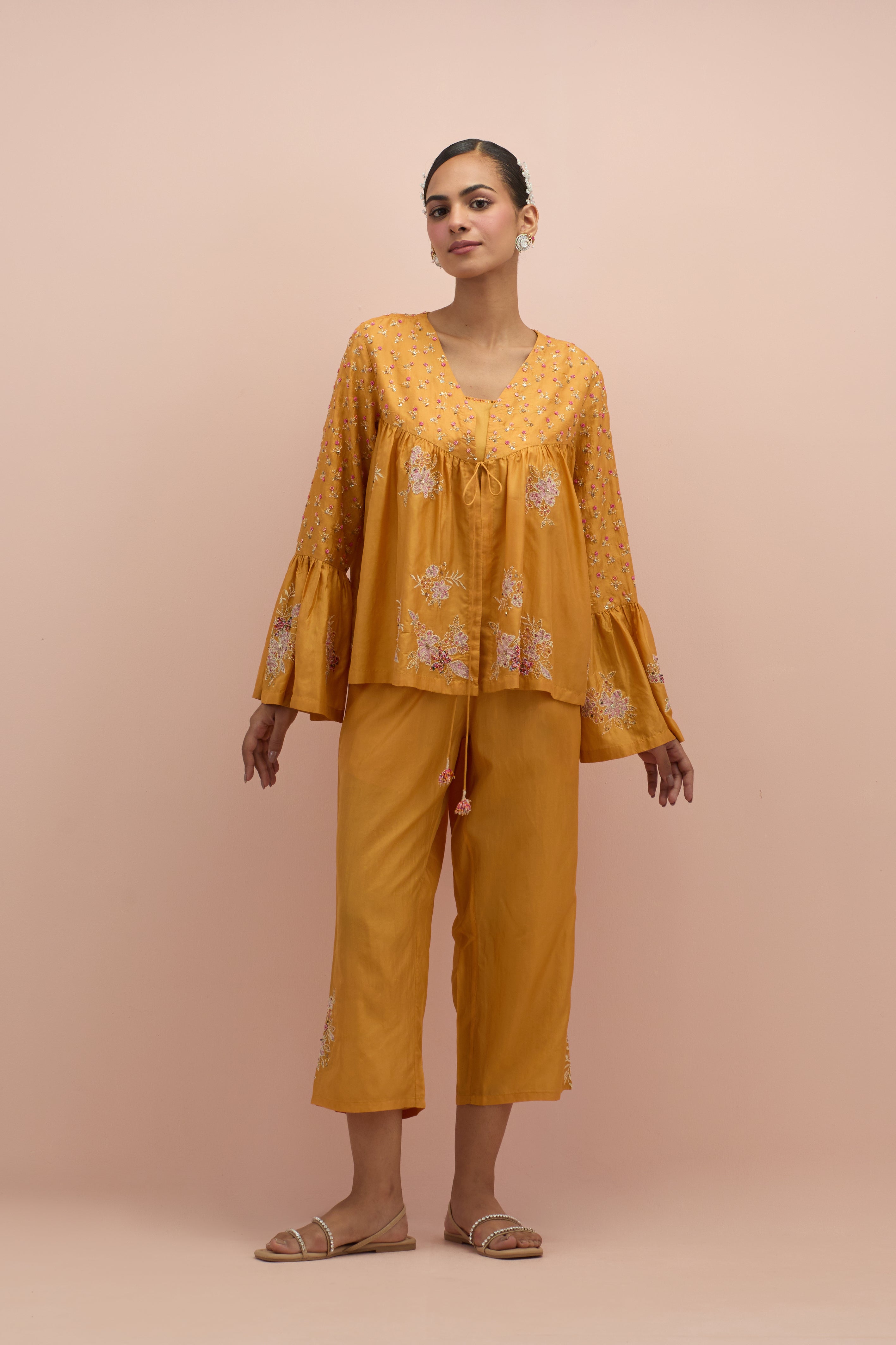 Amber silk short top with hand block printed appliqué motifs and delicate embroidered flowers, highlighted with sequins and multi-colored beads, paired with amber silk ankle length straight pants.