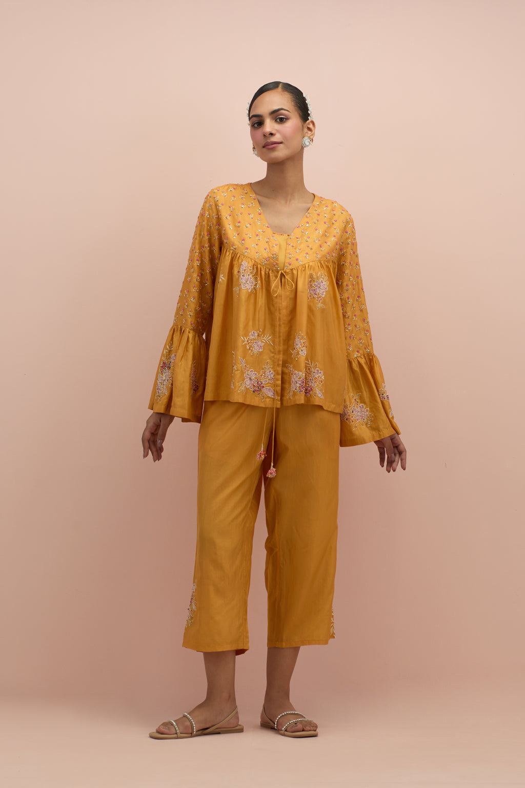 Amber silk short top with hand block printed appliqué motifs and delicate embroidered flowers, highlighted with sequins and multi-colored beads, paired with amber silk ankle length straight pants.