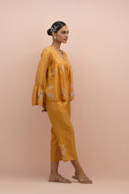 Amber silk short top with hand block printed appliqué motifs and delicate embroidered flowers, highlighted with sequins and multi-colored beads, paired with amber silk ankle length straight pants.