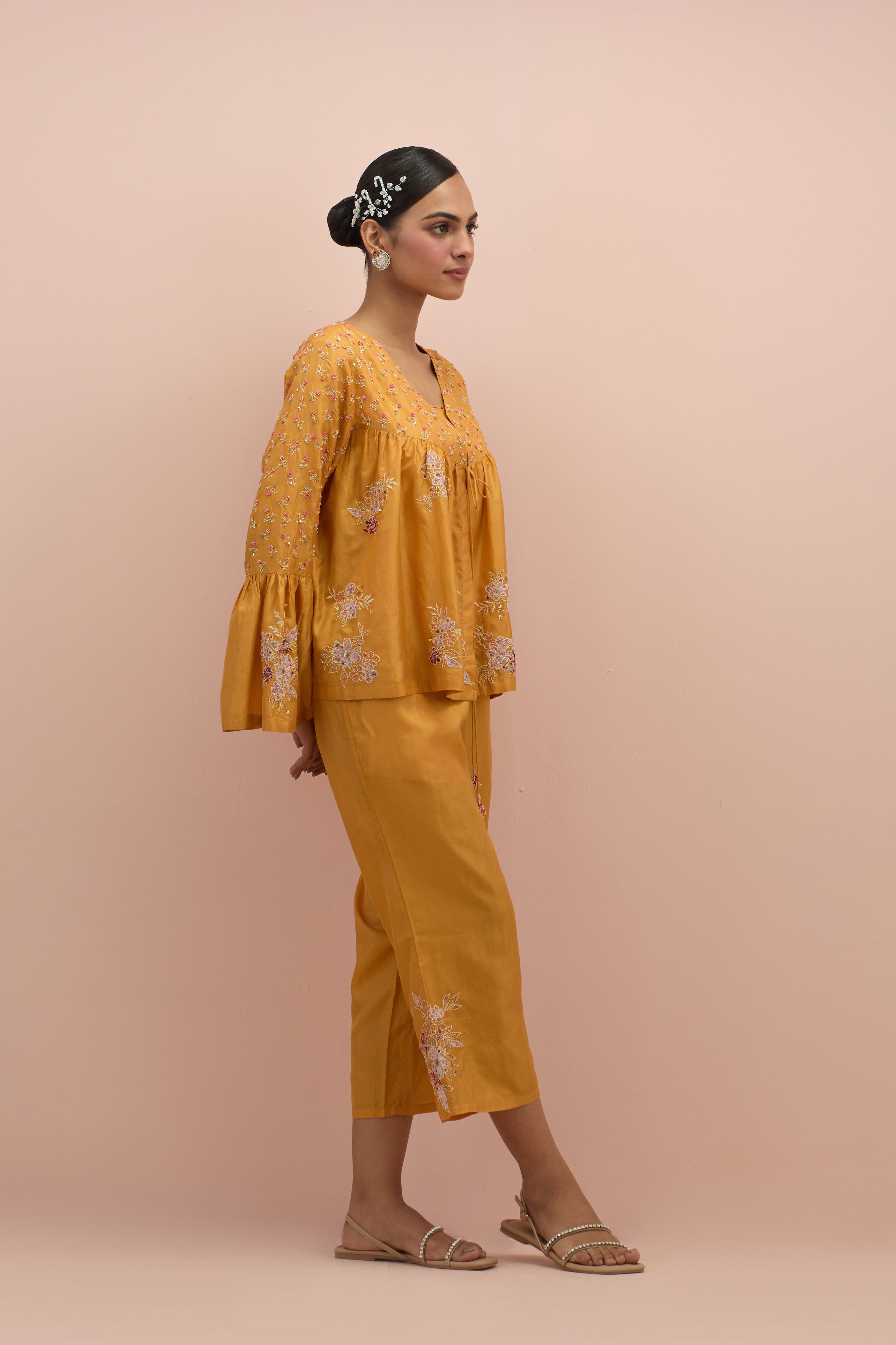 Amber silk short top with hand block printed appliqué motifs and delicate embroidered flowers, highlighted with sequins and multi-colored beads, paired with amber silk ankle length straight pants.