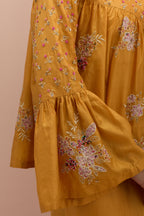 Amber silk short top with hand block printed appliqué motifs and delicate embroidered flowers, highlighted with sequins and multi-colored beads, paired with amber silk ankle length straight pants.