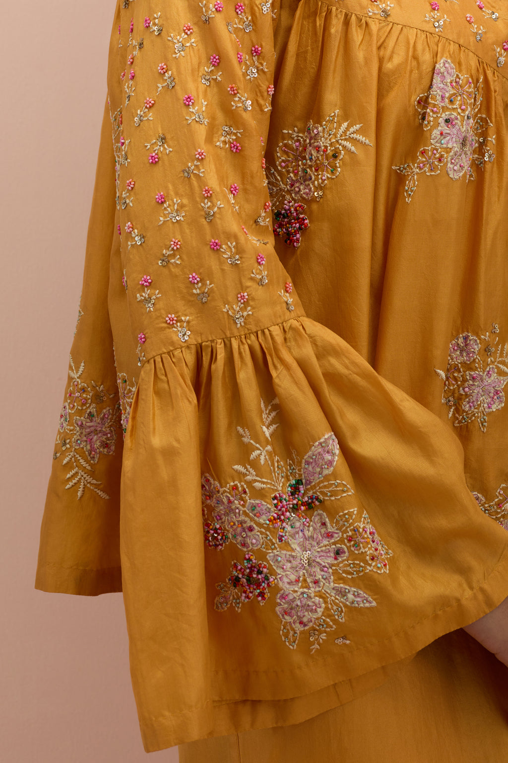 Amber silk short top with hand block printed appliqué motifs and delicate embroidered flowers, highlighted with sequins and multi-colored beads, paired with amber silk ankle length straight pants.