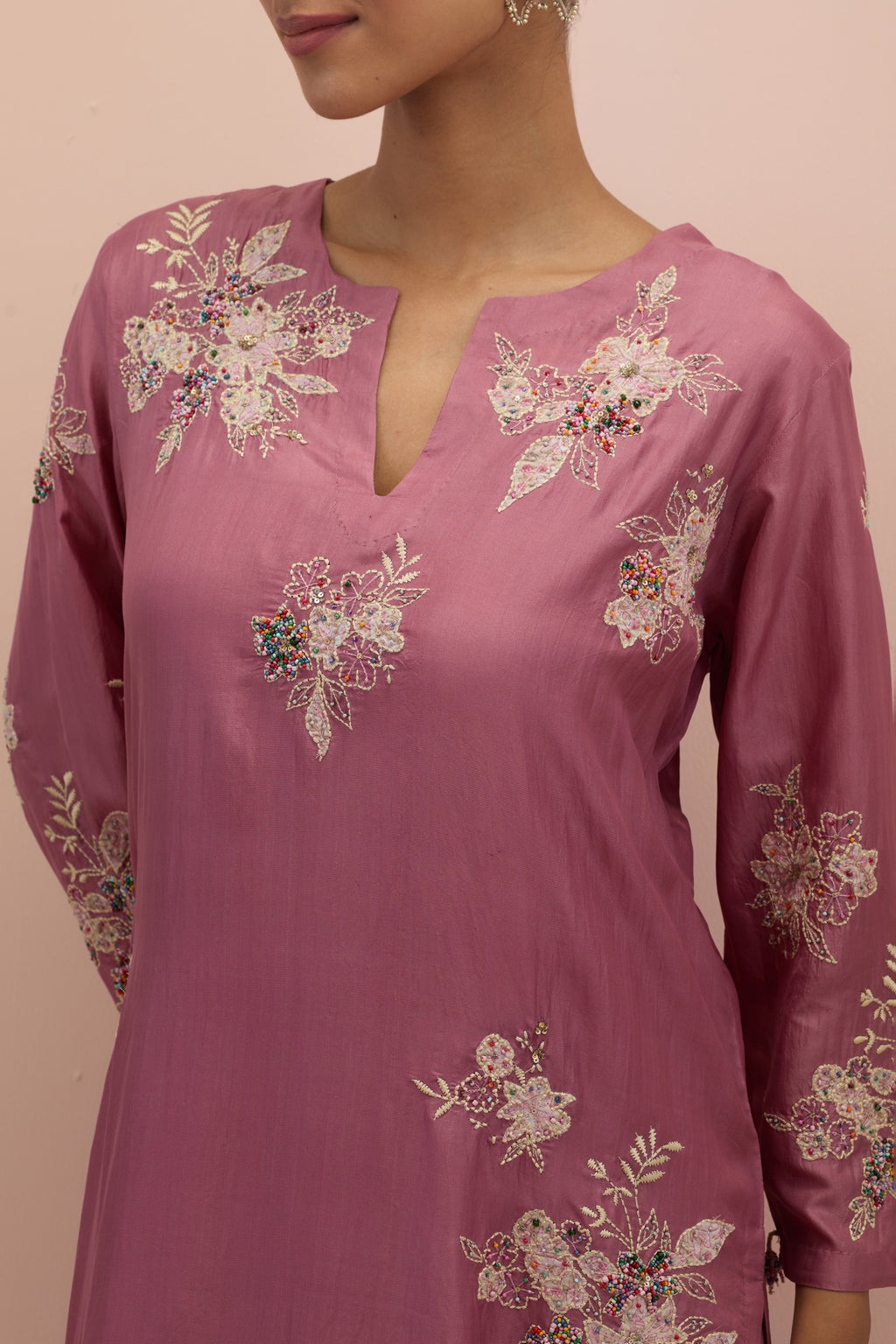 Salmon pink silk straight kurta set with randomly placed hand block printed appliquéd flowers, highlighted with sequins and multi-colored beads.