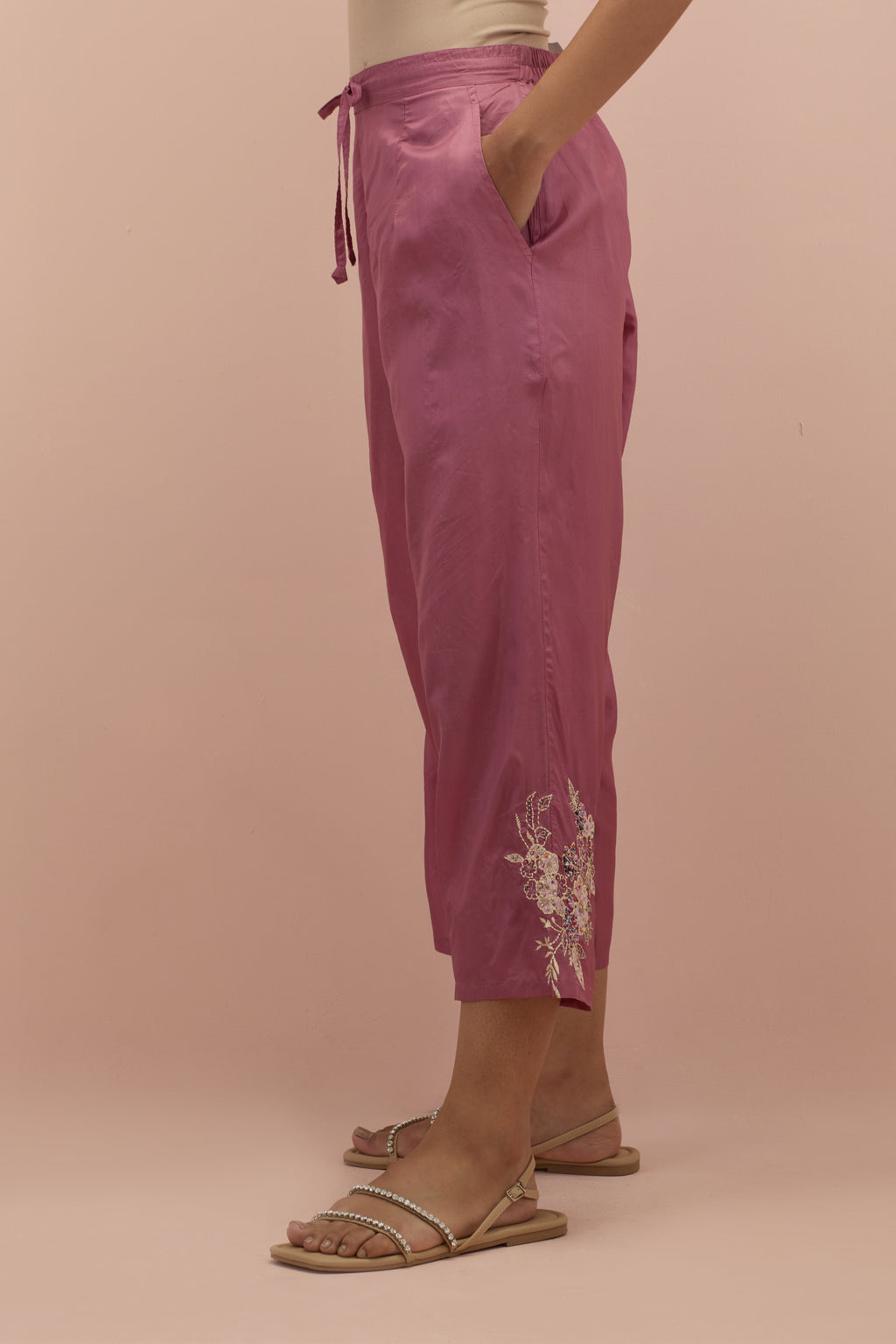 Salmon pink silk ankle length straight pants with hand block printed appliqué motifs at the sides, highlighted with sequins and multi-colored beads.