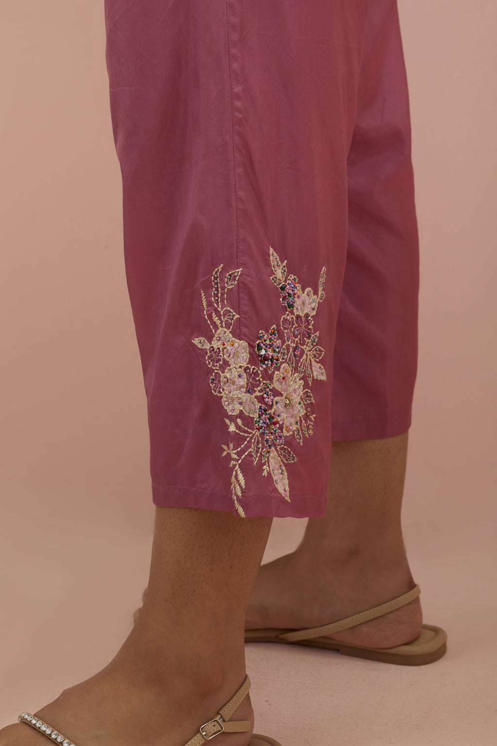 Salmon pink silk ankle length straight pants with hand block printed appliqué motifs at the sides, highlighted with sequins and multi-colored beads.