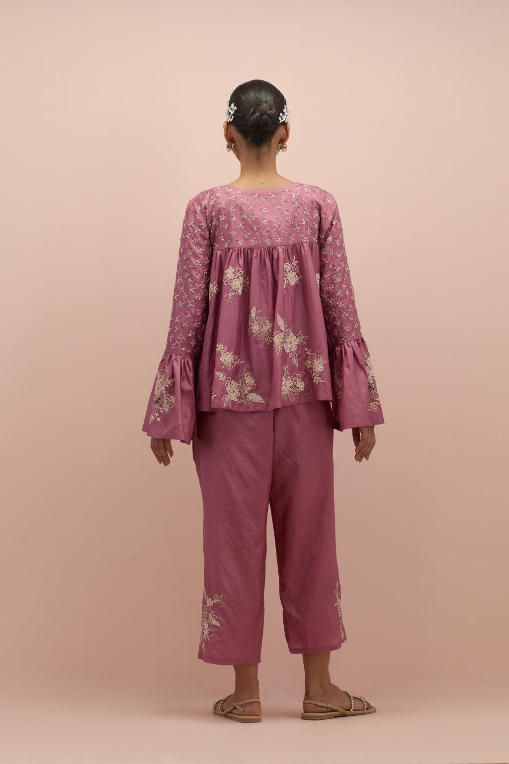 Salmon pink silk short top with hand block printed appliqué motifs and delicate embroidered flowers, highlighted with sequins and multi-colored beads, paired with salmon pink silk ankle length straight pants.