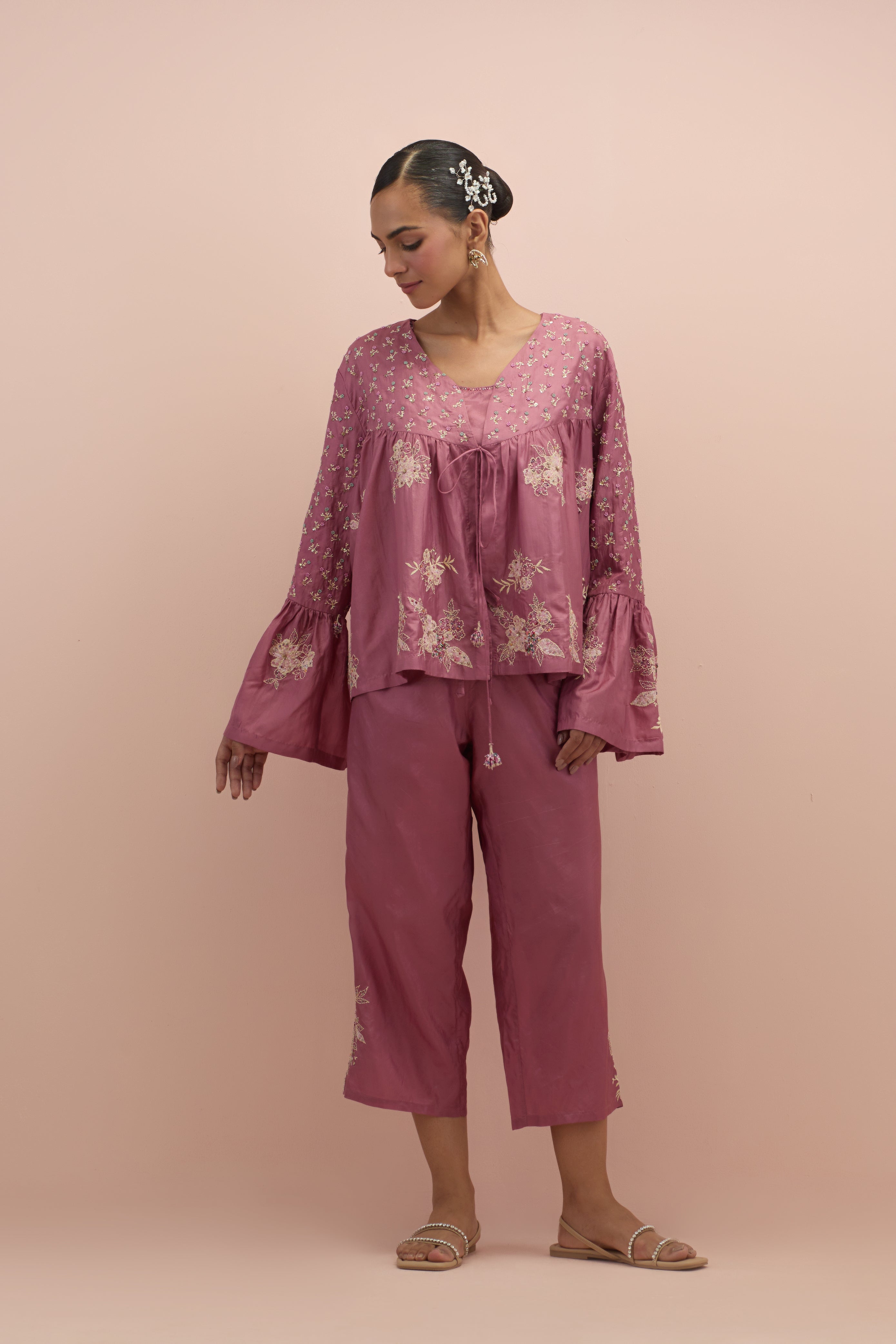 Salmon pink silk short top with hand block printed appliqué motifs and delicate embroidered flowers, highlighted with sequins and multi-colored beads, paired with salmon pink silk ankle length straight pants.