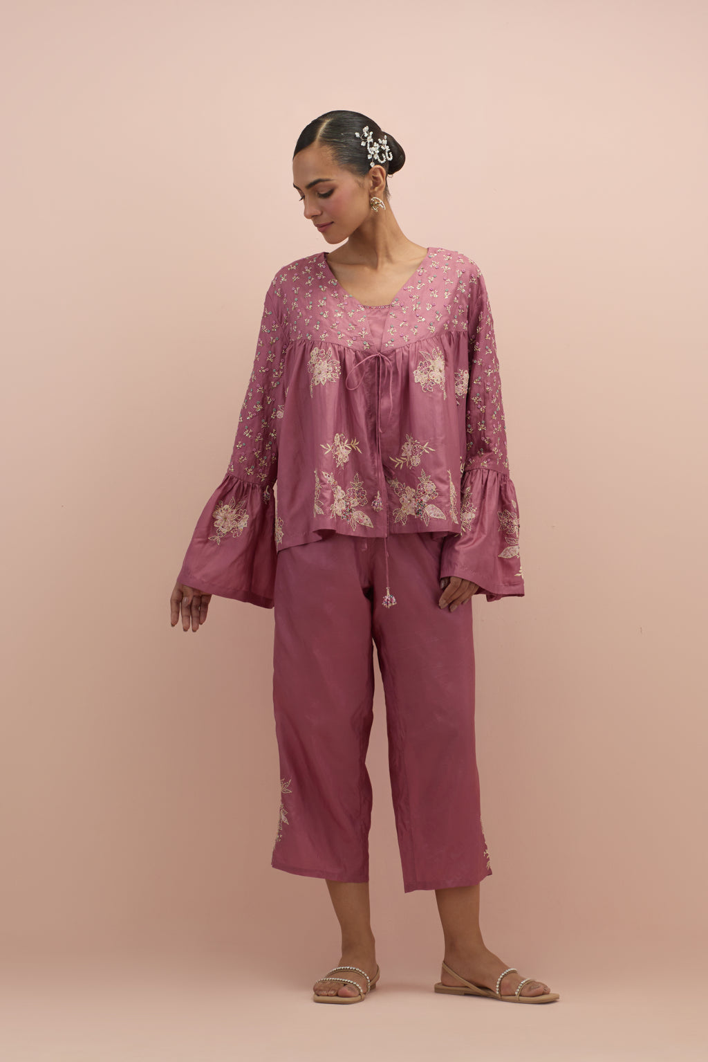 Salmon pink silk short top with hand block printed appliqué motifs and delicate embroidered flowers, highlighted with sequins and multi-colored beads, paired with salmon pink silk ankle length straight pants.