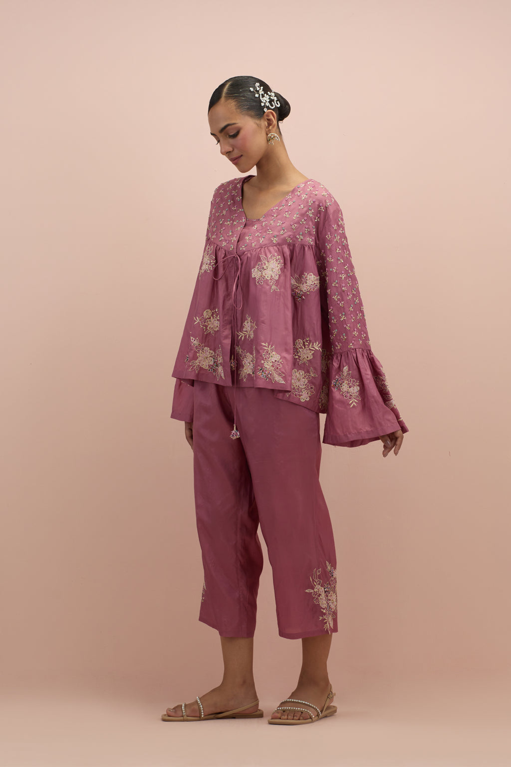 Salmon pink silk short top with hand block printed appliqué motifs and delicate embroidered flowers, highlighted with sequins and multi-colored beads, paired with salmon pink silk ankle length straight pants.