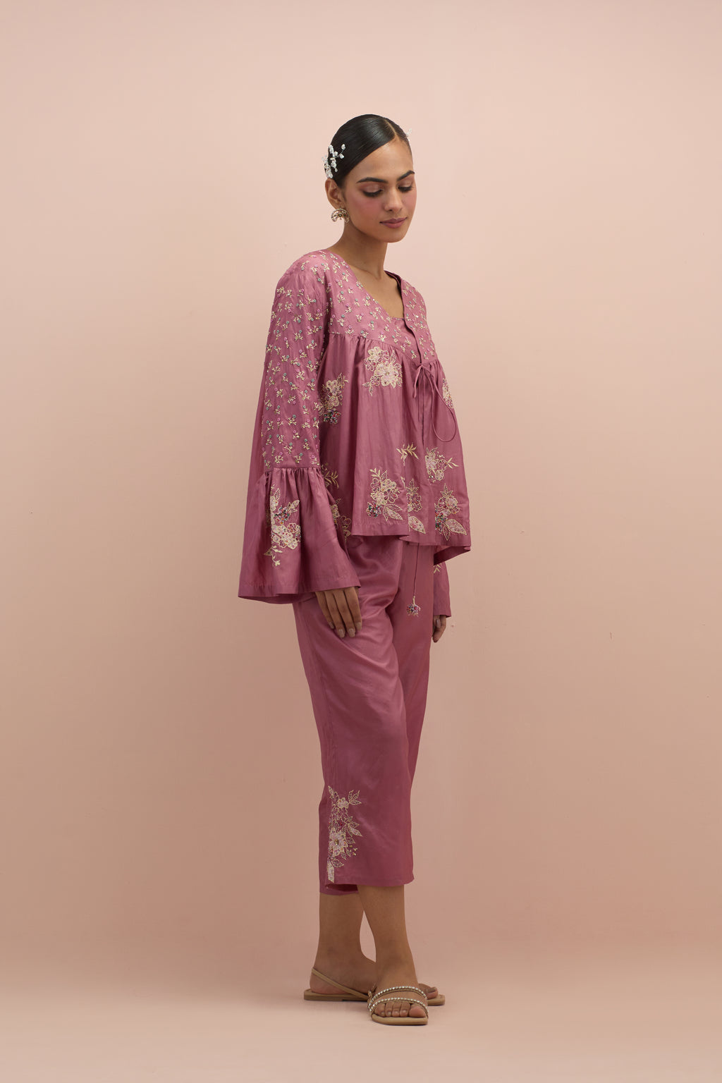 Salmon pink silk short top with hand block printed appliqué motifs and delicate embroidered flowers, highlighted with sequins and multi-colored beads, paired with salmon pink silk ankle length straight pants.