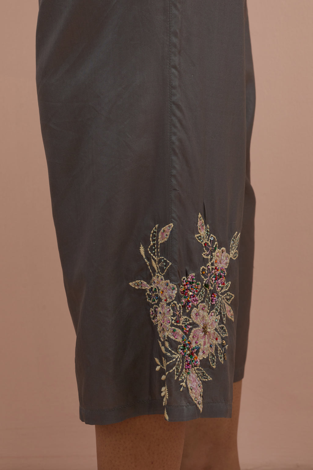 Iron grey silk ankle length straight pants with hand block printed appliqué motifs at the sides, highlighted with sequins and multi-colored beads.