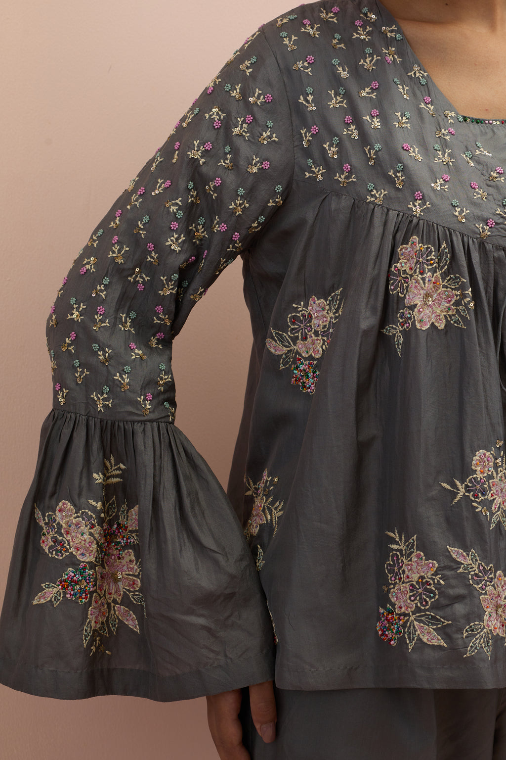 Iron grey silk short top with hand block printed appliqué motifs and delicate embroidered flowers, highlighted with sequins and multi-colored beads, paired with iron grey silk ankle length straight pants.