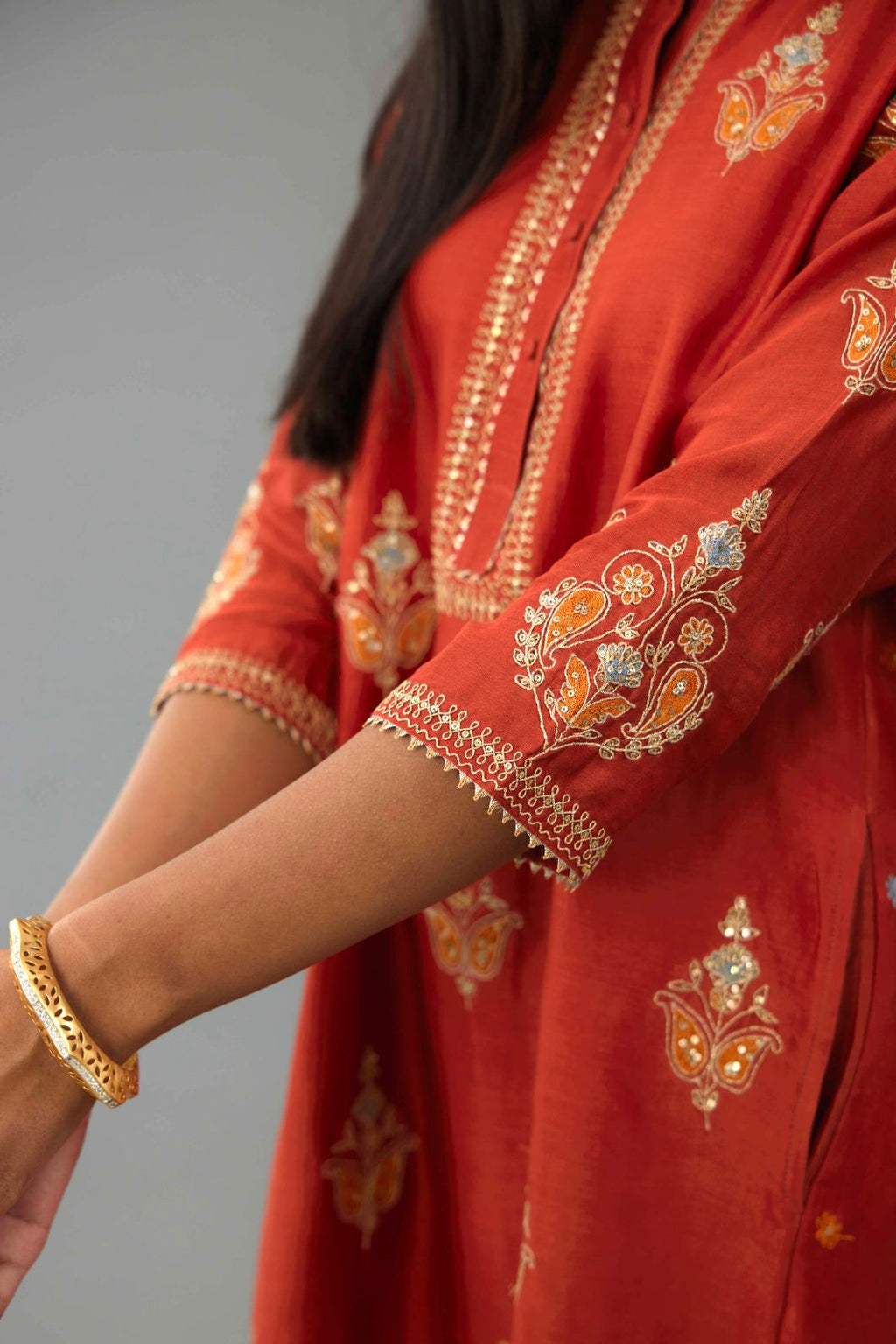 Rust silk chanderi A-line short kurta set with dori and contrast silk thread embroidery, highlighted with gold sequins work.