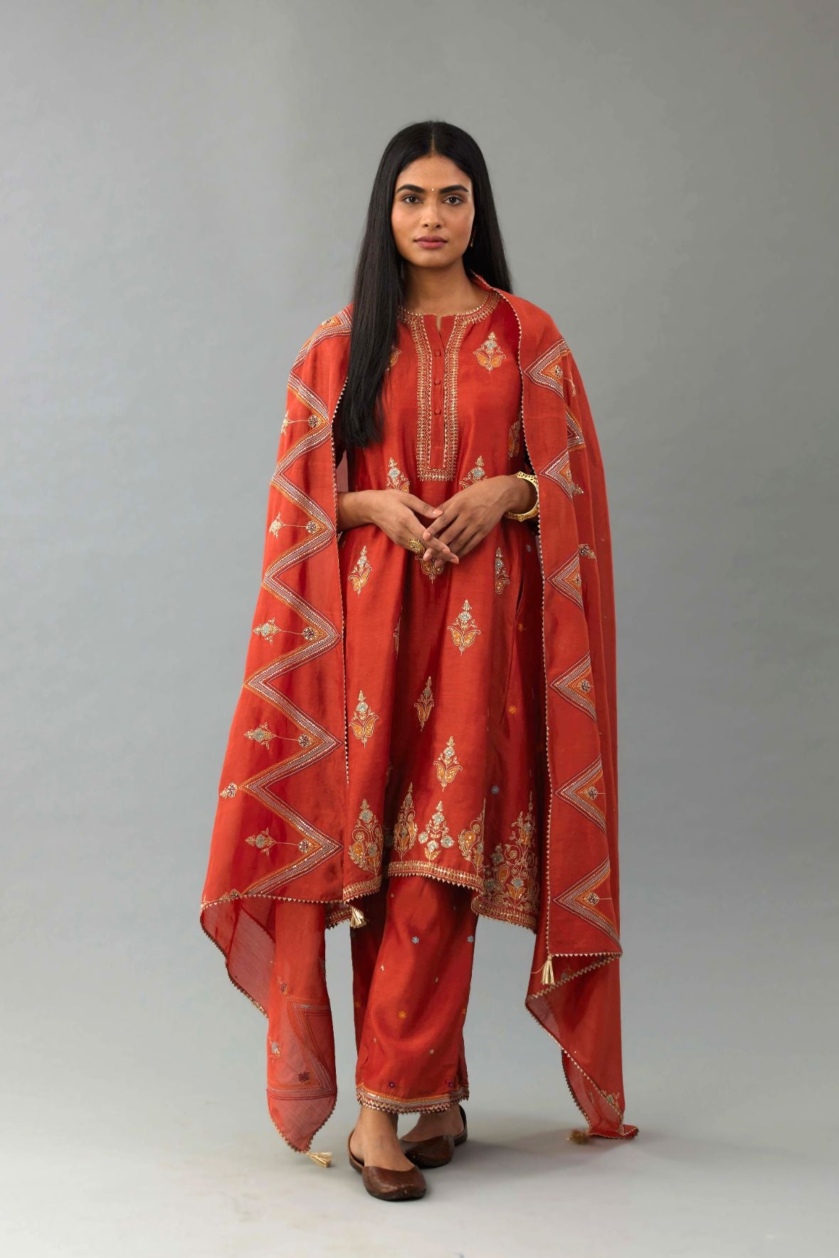 Rust silk chanderi A-line short kurta set with dori and contrast silk thread embroidery, highlighted with gold sequins work.