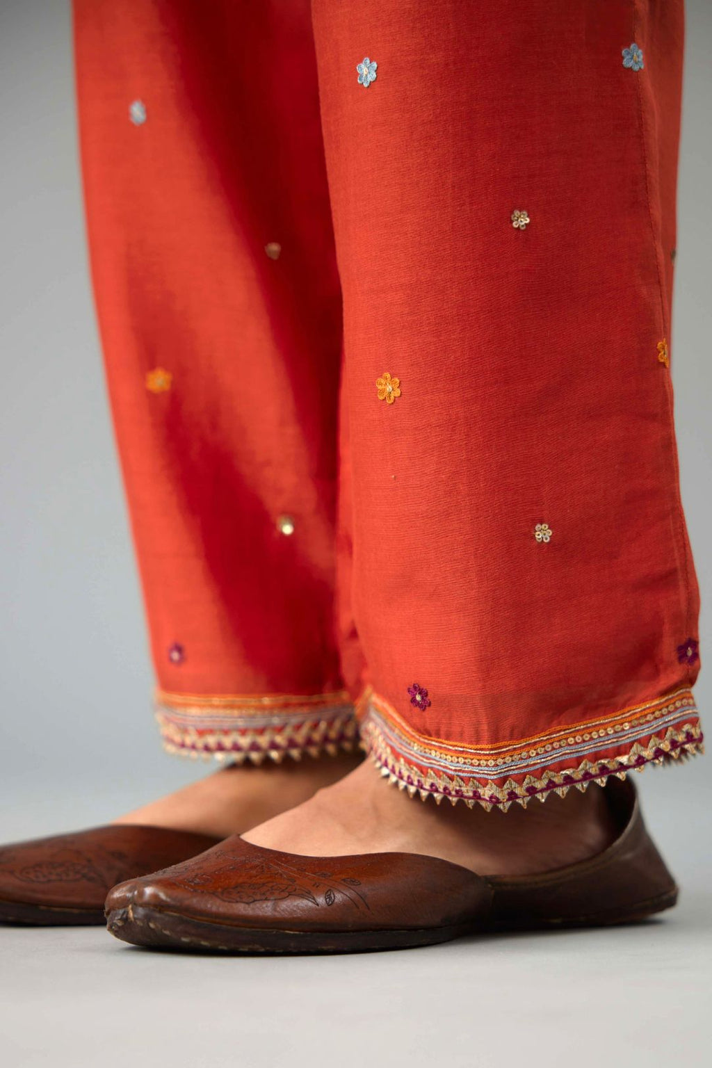 Rust silk chanderi straight pants with dori and contrast silk thread embroidery,  detailed with gold sequins work.
