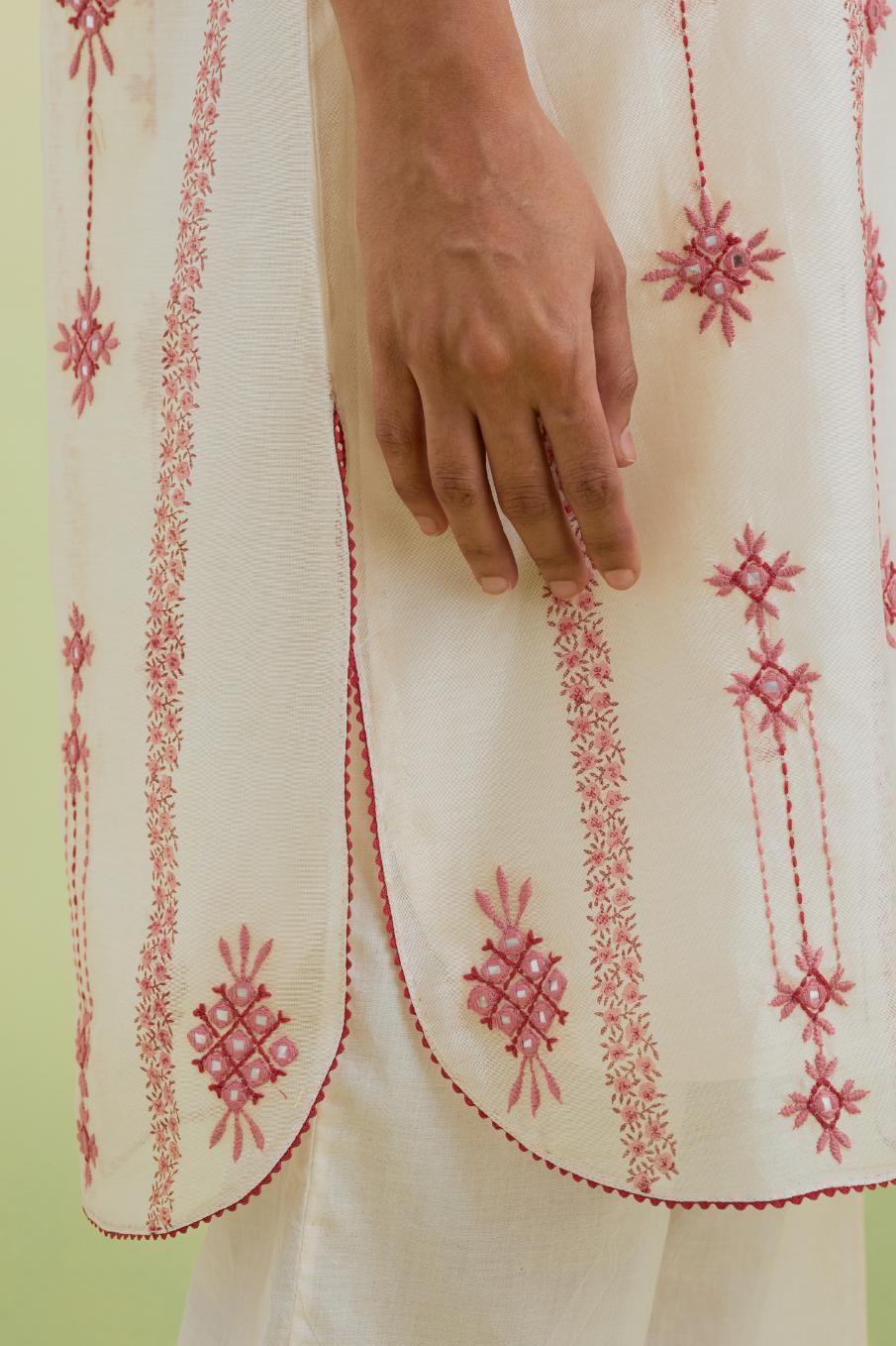 Pink and off-white hand block printed silk chanderi straight short kurta with thread and mirror embroidery along with kantha work, paired with off white straight ankle length pants with pink colored hand-block printed border at hem.