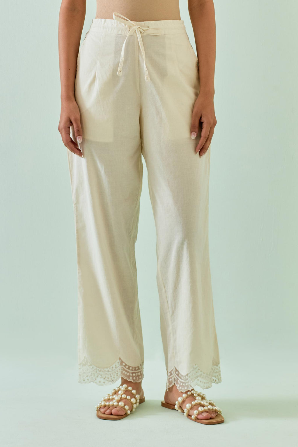 Off white straight pants with scalloped embroidery at bottom hem.