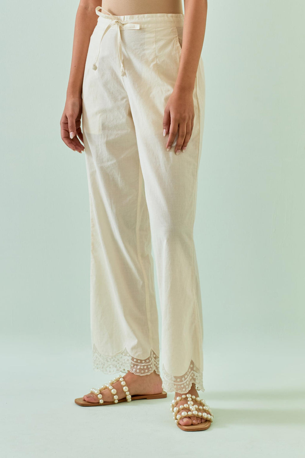 Off white straight pants with scalloped embroidery at bottom hem.