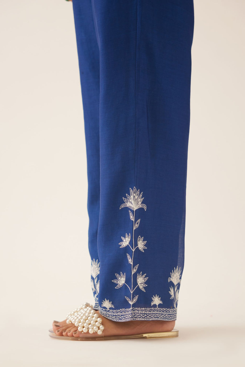 Blue silk chanderi straight pants with off white silk thread embroidery at hem.