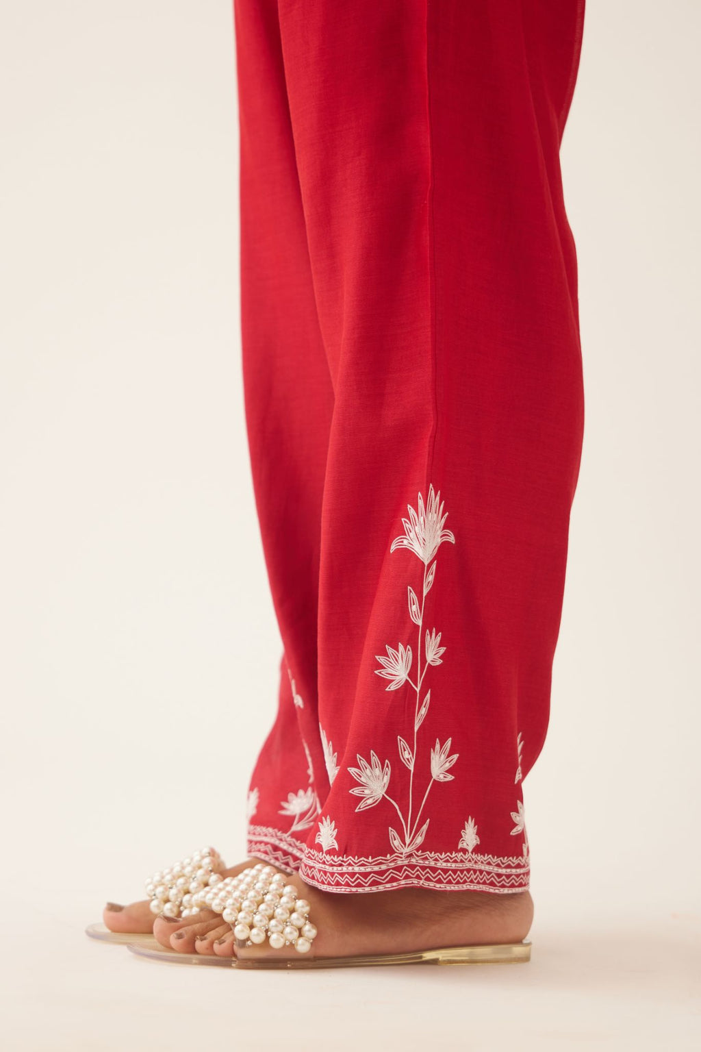 Red silk chanderi straight pants with off white silk thread embroidery at hem.