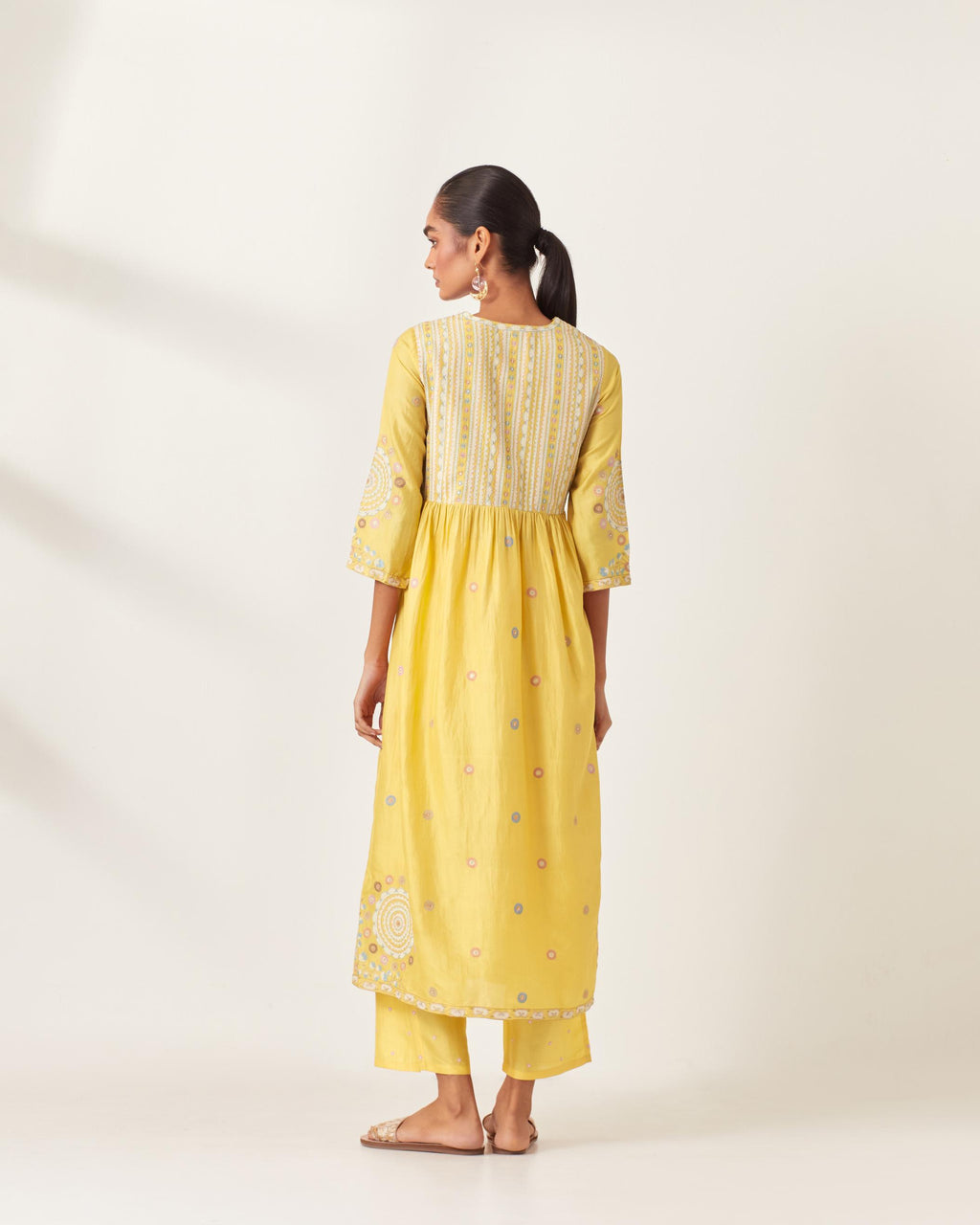 Yellow silk kurta dress set with appliqué stripes along with aari threadwork flowers and floral trellises along with a circular appliqued motif and fine gathers at empire line.