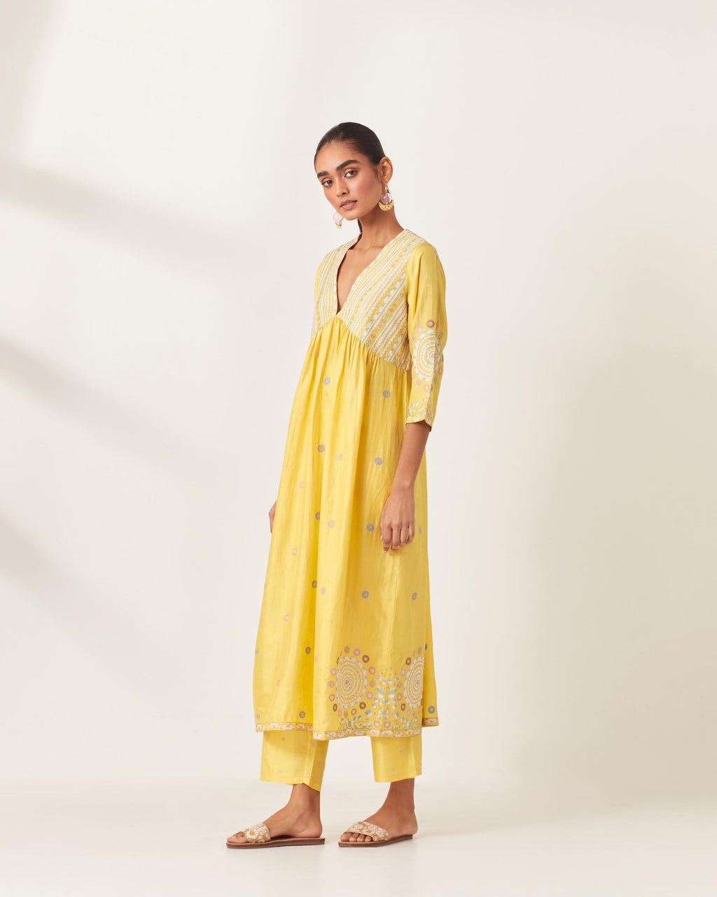 Yellow silk kurta dress set with appliqué stripes along with aari threadwork flowers and floral trellises along with a circular appliqued motif and fine gathers at empire line.