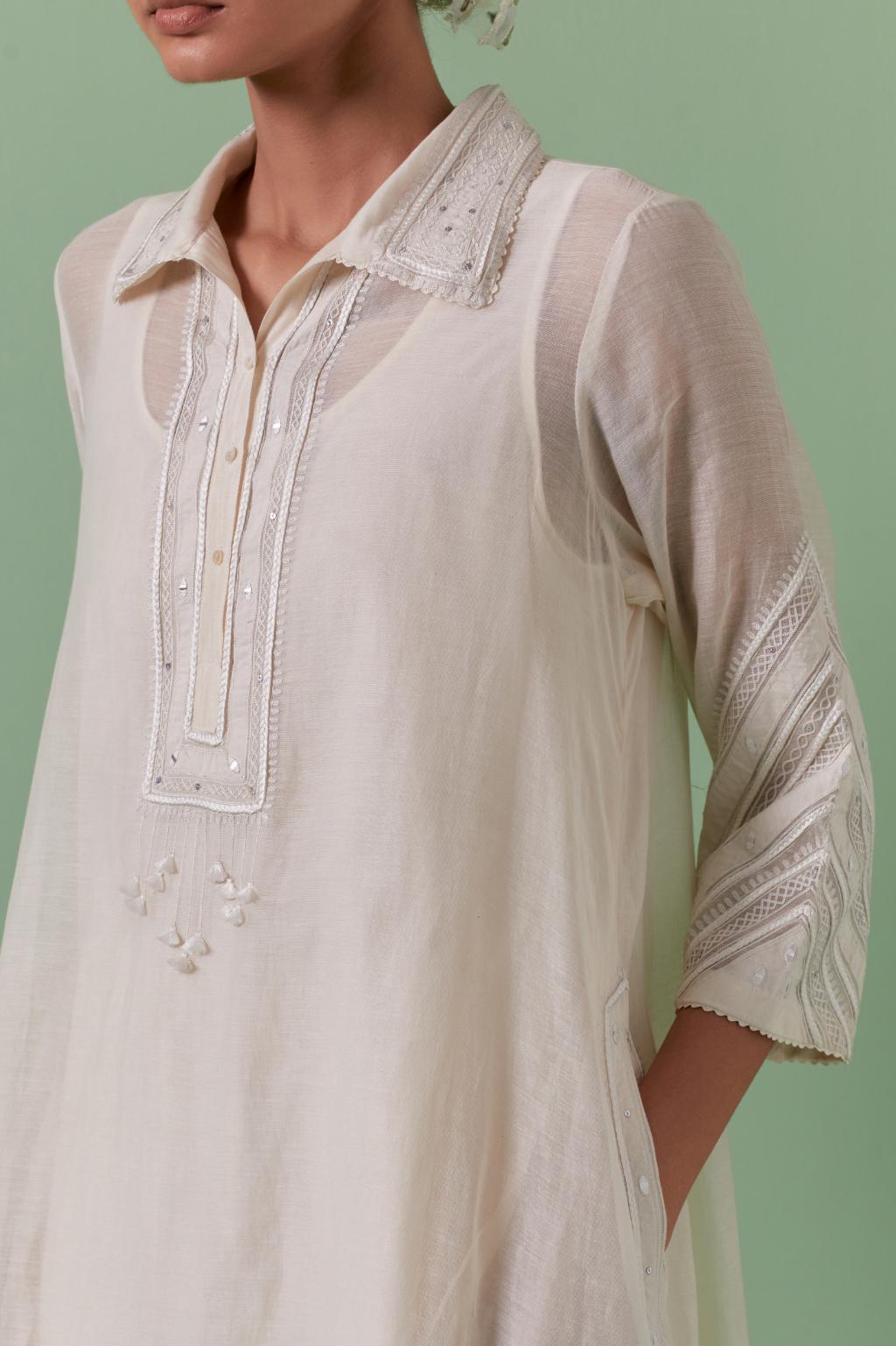 Off white cotton chanderi A-line kurta set with collar, detailed with patchwork, silk thread embroidery, mirrors, sequins and tassels.