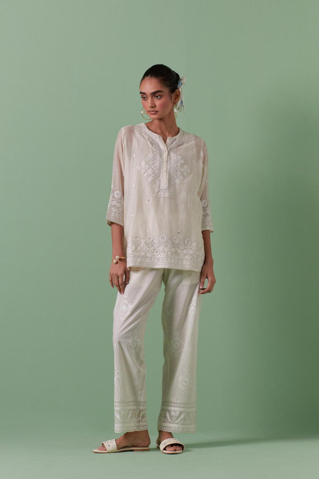 Off-white cotton chanderi embroidered short top with 3/4th sleeves, paired with off white cotton straight pants with all over off white color embroidery detailed with sequins.