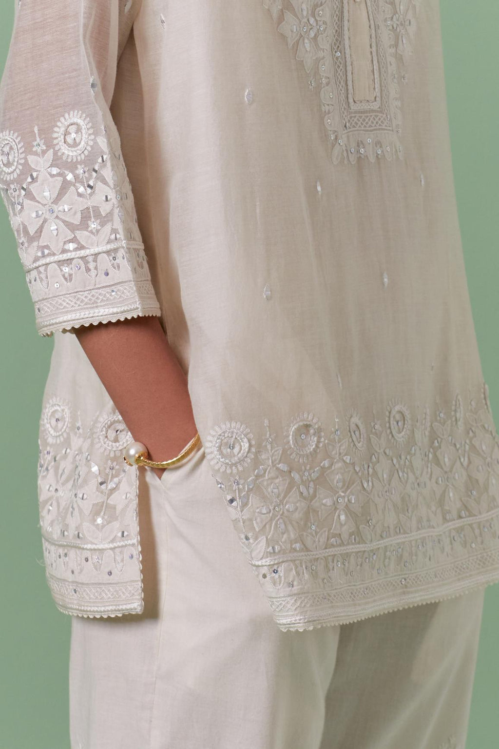 Off-white cotton chanderi embroidered short top with 3/4th sleeves, paired with off white cotton straight pants with all over off white color embroidery detailed with sequins.